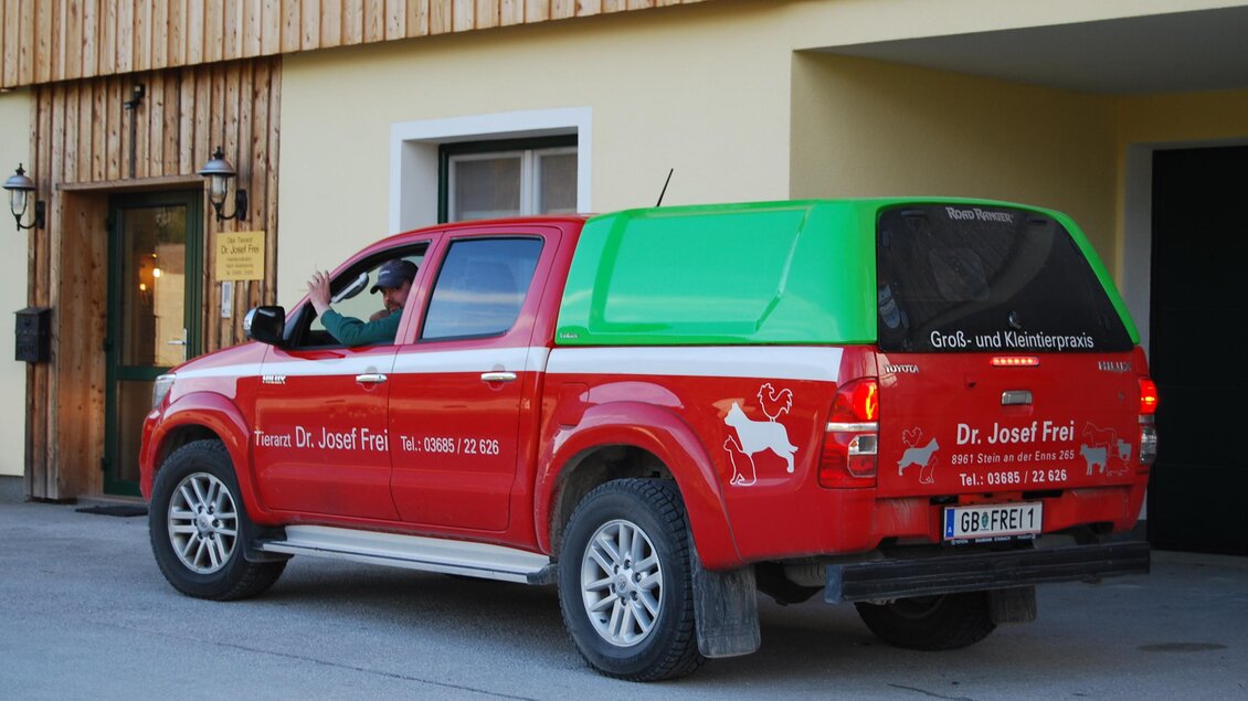 Ein roter Pickup mit einem grünen Aufsatz steht vor einem Gebäude. Der Wagen ist mit einer Tierarztpraxis beschriftet. | © Dr. Josef Frei
