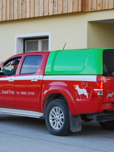 Ein roter Pickup mit einem grünen Aufsatz steht vor einem Gebäude. Der Wagen ist mit einer Tierarztpraxis beschriftet. | © Dr. Josef Frei