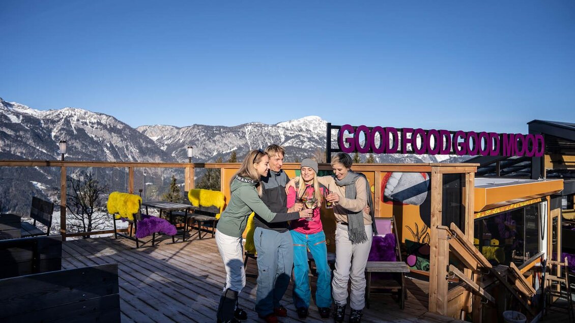 Eine Gruppe von vier skifahrenden Freunden steht auf einer Terrasse mit Bergen im Hintergrund. Sie genießen die Zeit in der Sonne und haben Spaß miteinander. | © Hotel Höflehner