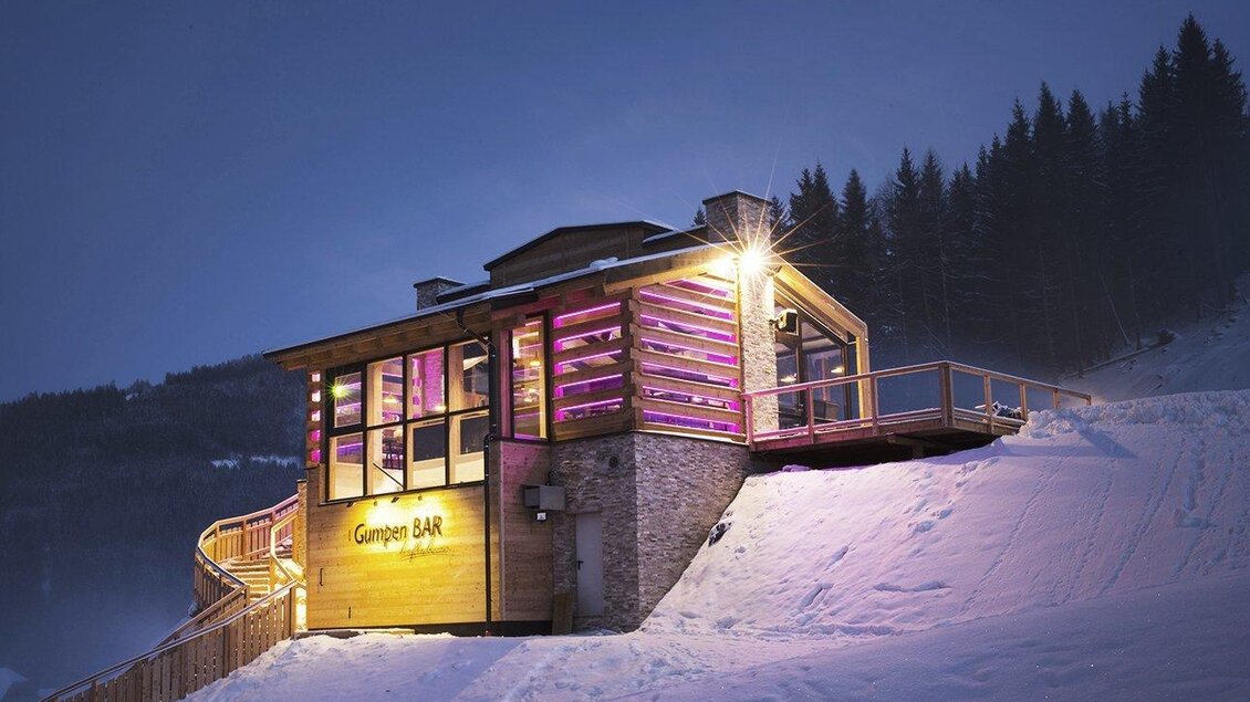 Eine moderne Skihütte mit beleuchteten Fenstern, umgeben von Schnee und Tannen. Die Hütte bietet eine gemütliche Atmosphäre in der Abenddämmerung. | © Hotel Höflehner