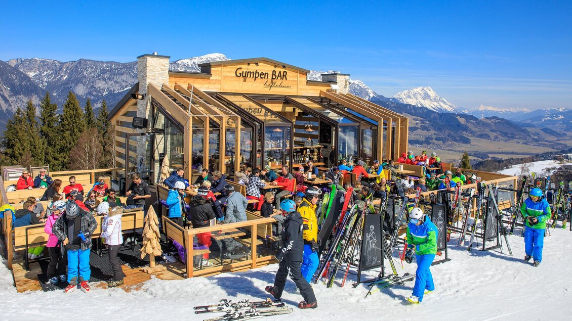 Eine lebhafte Skihütte mit vielen Gästen und einer wunderschönen Berglandschaft. Der Schnee und die umliegenden Berge schaffen eine winterliche Atmosphäre. | © AlmSkiHütten am Hauser Kaibling@MartinHuber