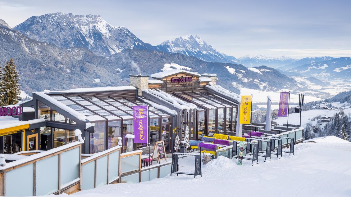Außenansicht der Gumpenbar am Hauser Kaibling mit Glasfront, Panoramaterrasse und Blick auf die verschneiten Berge. | © Gumpenbar