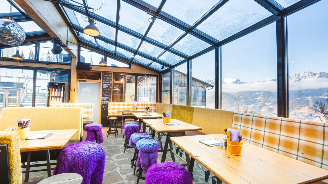 Modern eingerichtete Gumpenbar mit Panoramafenstern und bunten Hockern mit lilafarbenen Sitzüberzügen. | © Gumpenbar