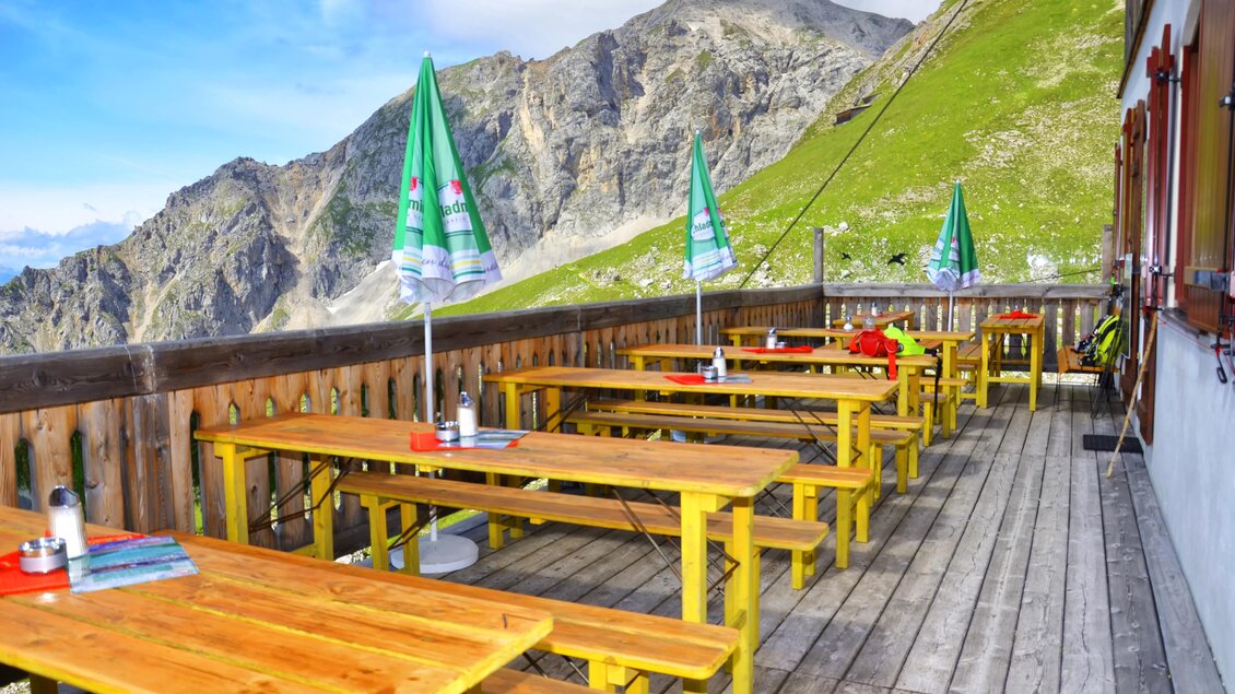 Eine gemütliche Terrasse mit Holztischen und Bänken in den Bergen. Die grünen Sonnenschirme bieten Schatten und der Ausblick ist atemberaubend. | © René Eduard Perhab