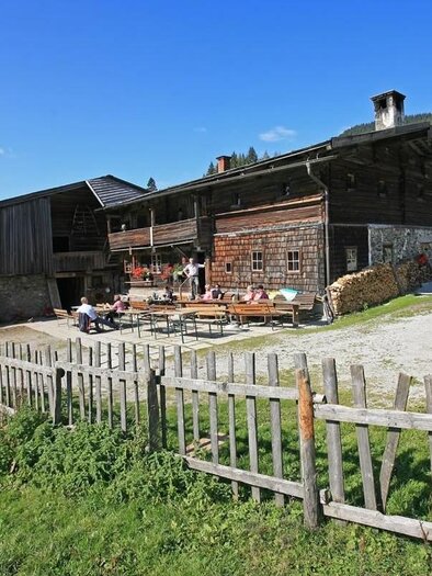 A traditional farm with wooden buildings and a clear blue sky.  
Surrounded by green meadows and a fence. | © Halseralm