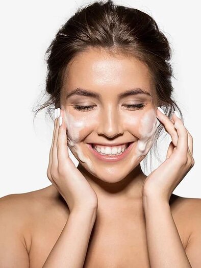 Eine lächelnde Frau reinigt ihr Gesicht mit Schaum. Sie zeigt eine gesunde, strahlende Haut. | © Hautwerkstatt by Milena