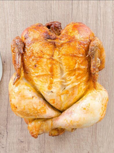 Ganzes gebratenes Hendl liegt auf einem Holztisch, daneben Messer und Gabel. | © Symbolbild