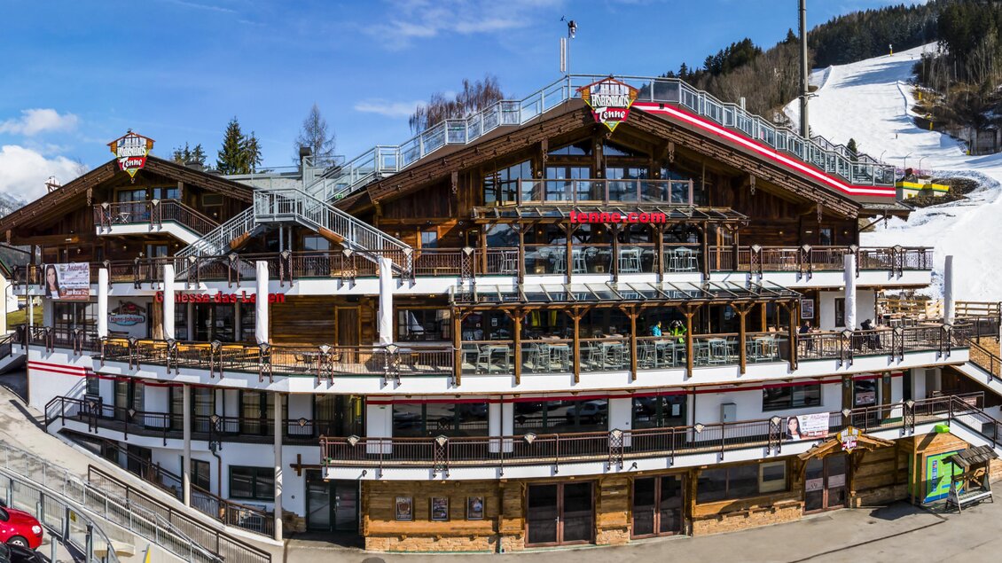 Ein gemütliches Ferienhaus in den Bergen mit Blick auf eine Skipiste. Die Umgebung ist schneebedeckt und der Himmel ist blau mit einigen Wolken. | © AIR-Media.at