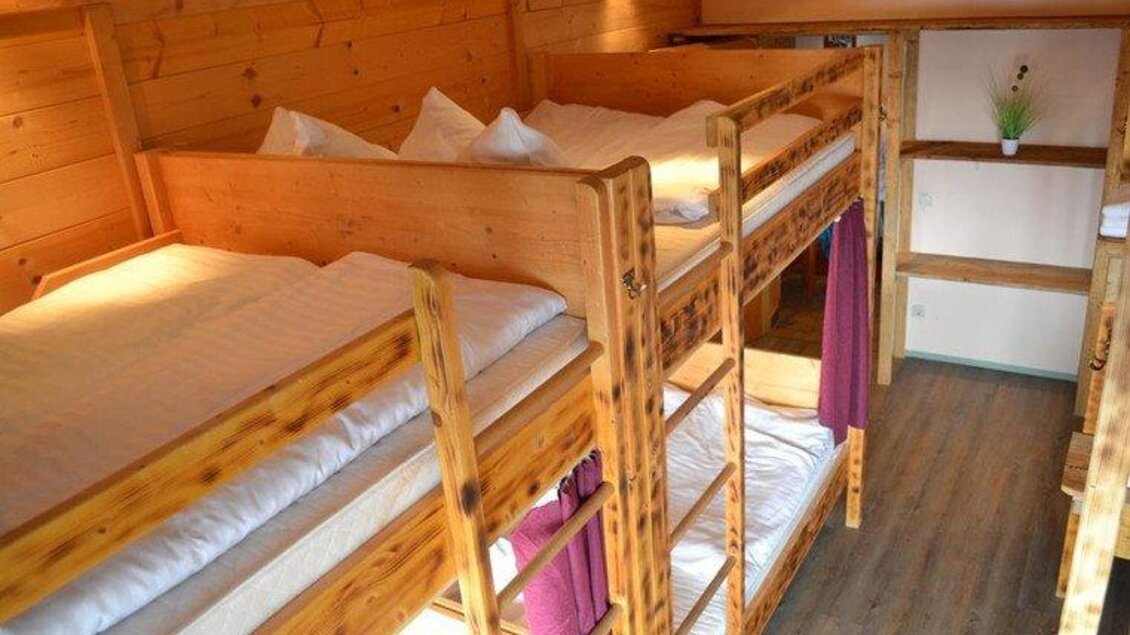 Ein gemütlicher Schlafraum mit zwei Etagenbetten aus Holz. Die hellen Wände und das frisch bezogene Bettzeug schaffen eine einladende Atmosphäre. | © Hoo-Ruck Alm