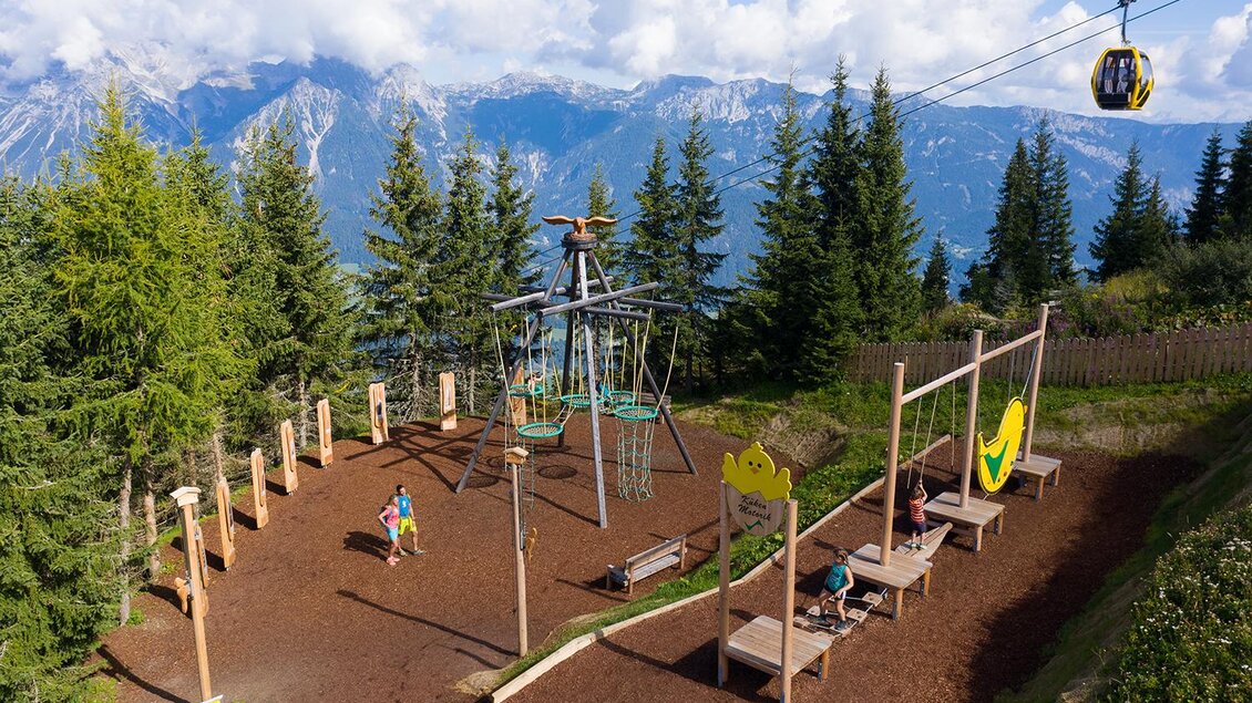 Ein Spielplatz in den Bergen mit einer Seilbahn im Hintergrund. Umgeben von Bäumen und einer schönen Berglandschaft. | © Josh Absenger