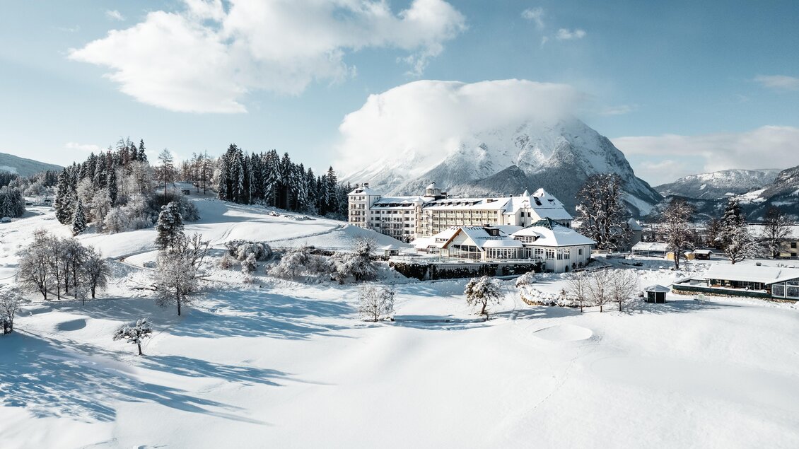 Eine verschneite Landschaft mit einem großen Berg im Hintergrund. Im Vordergrund steht ein charmantes Hotel, umgeben von schneebedeckten Bäumen. | © Thomas Sattler