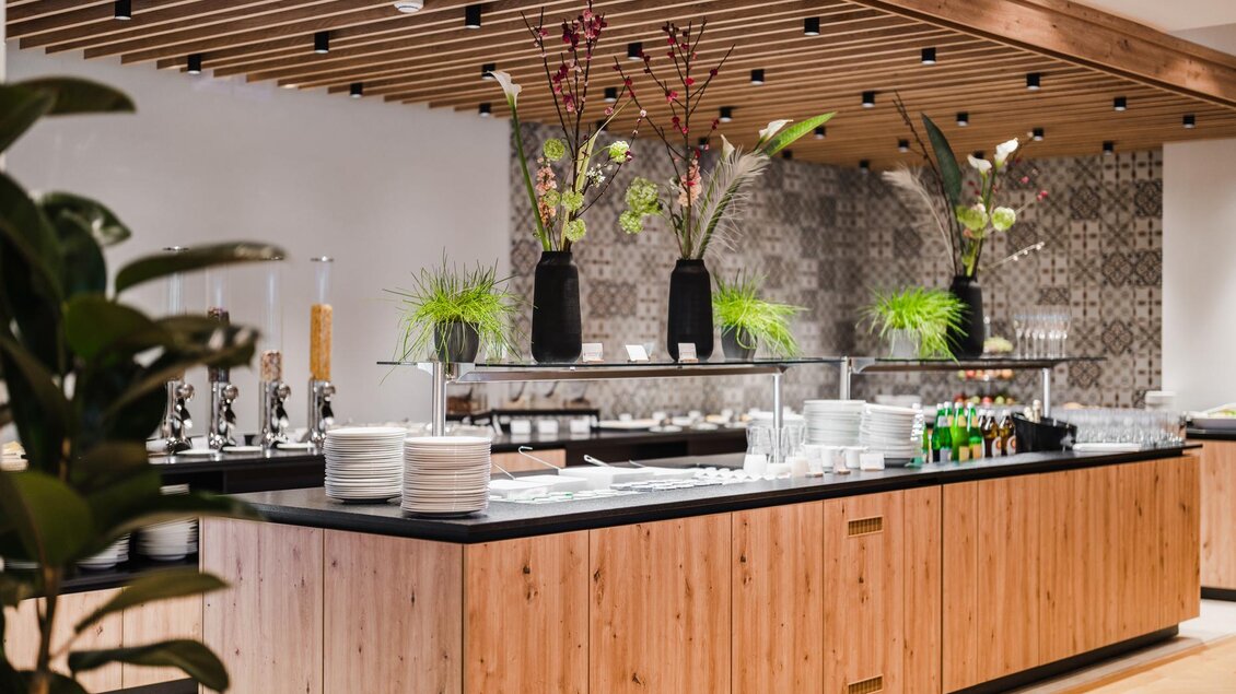 Ein eleganter Buffetbereich mit Holzoberflächen und dekorativen Pflanzen. Auf dem Tisch sind Teller, Gläser und Getränke angeordnet. | © Thomas Sattler