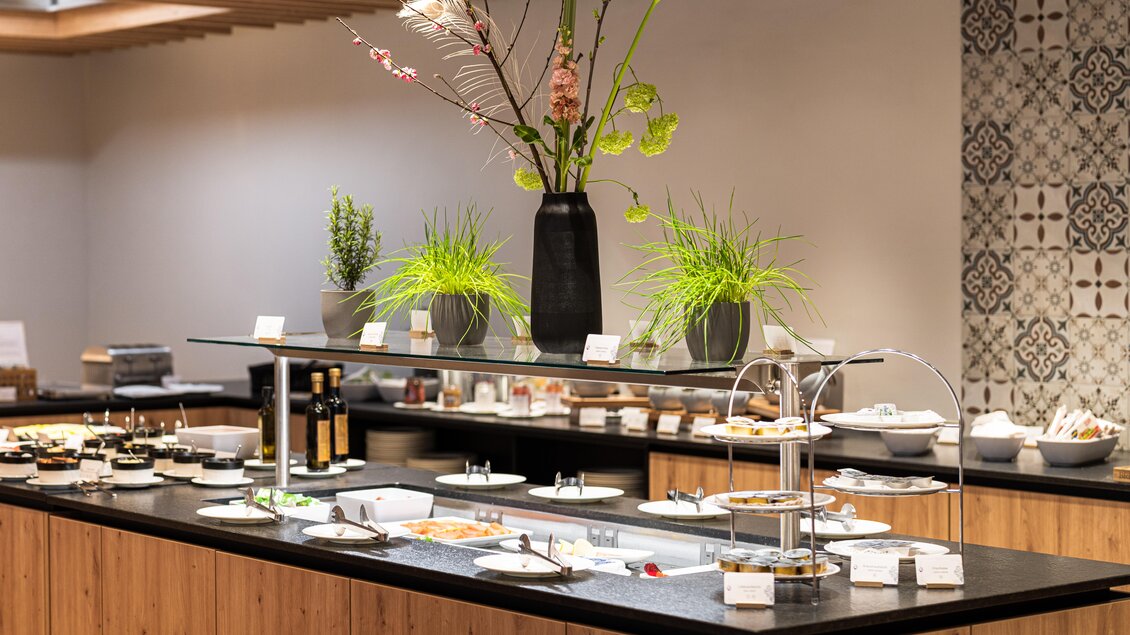 Ein eleganter Buffetbereich mit einer Vielzahl von Gerichten und frischen Kräutern in dekorativen Vasen. Die Holz- und Steinelemente schaffen eine einladende Atmosphäre. | © Thomas Sattler