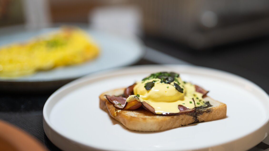 Ein Teller mit einem Toast, belegt mit Schinken und einem Spiegelei, das mit Hollandaise-Sauce übergossen ist. Im Hintergrund ist ein weiteres Gericht zu sehen. | © Thomas Sattler 