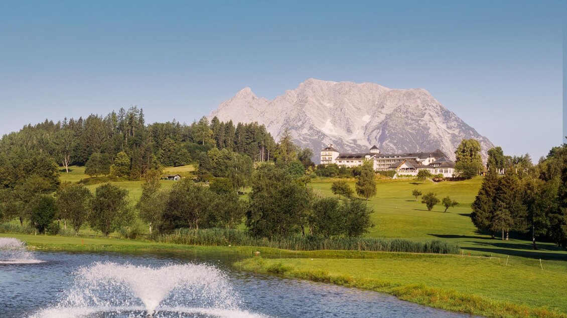 Eine ruhige Landschaft mit einem Teich und sprudelndem Wasser. Im Hintergrund erhebt sich ein beeindruckendes Gebirge unter blauem Himmel. | © Edy Gröger