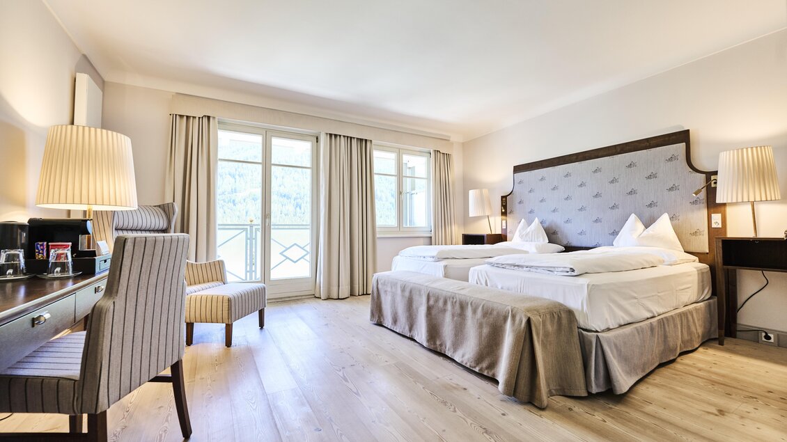 Ein modernes Hotelzimmer mit zwei Betten, einem Schreibtisch und einem gemütlichen Sessel. Große Fenster sorgen für viel Tageslicht und Blick auf die Umgebung. | © Thomas Sattler