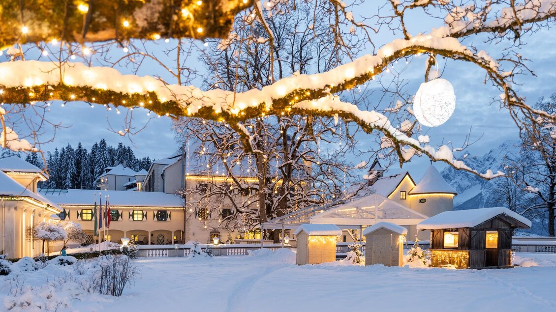 Eine verschneite Landschaft mit festlich beleuchteten Bäumen und einem eleganten Gebäude im Hintergrund. Die Szene strahlt eine ruhige, winterliche Atmosphäre aus. | © Thomas Sattler