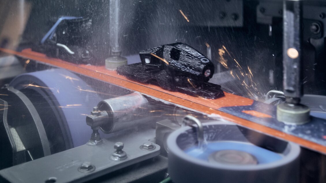 Ein industrielles Fertigungsumfeld mit Maschinen, die Teile bearbeiten. Funken fliegen, während ein schwarzes Teil auf einem Förderband bearbeitet wird. | © Intersport Gerhardter