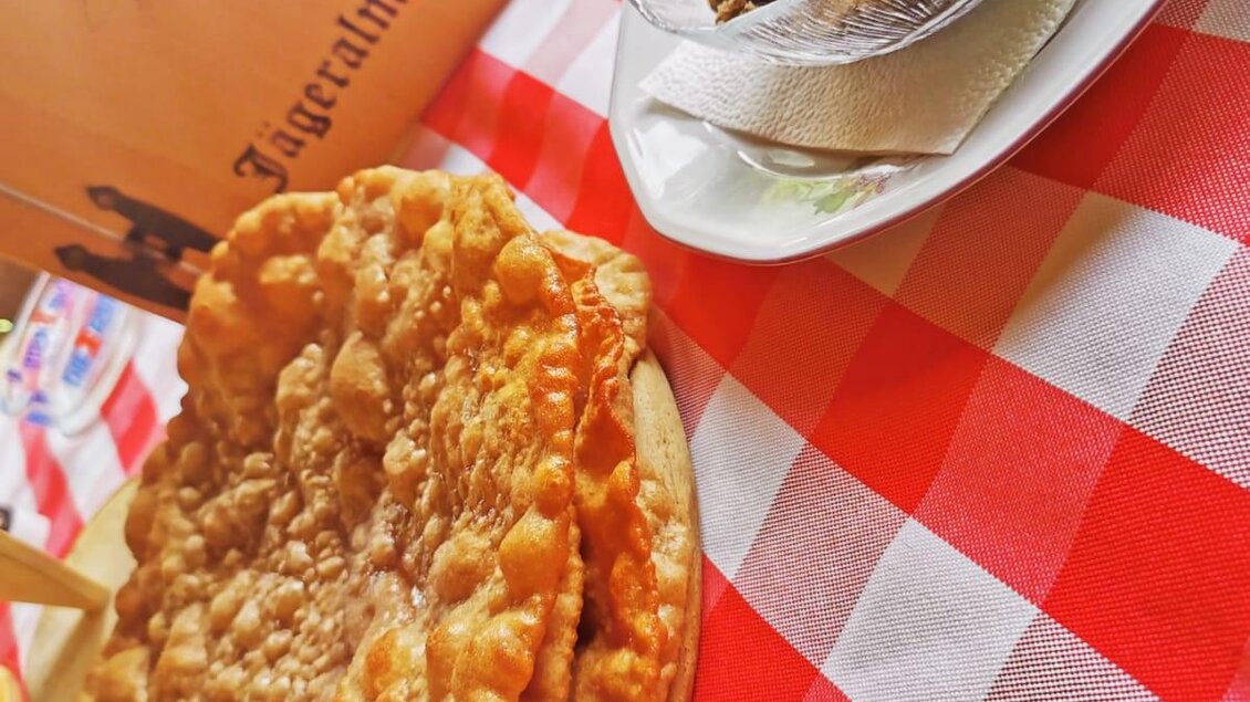 Ein Teller mit knusprigen, goldbraunen Teigprodukten liegt auf einem rot-weißen karierten Tischcloth. Nebenan befindet sich eine Schale mit süßer Füllung. | © Familie Moitzi