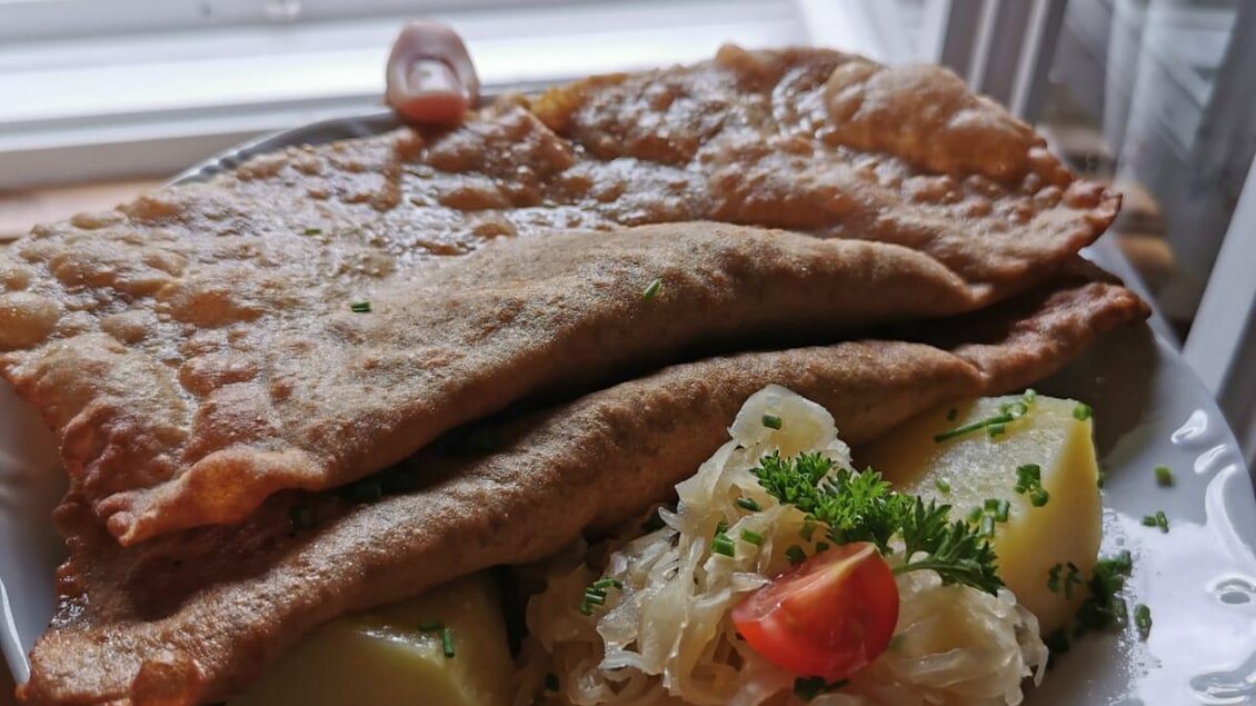 Ein Teller mit zwei knusprigen Pfannkuchen, Beilagen aus Kartoffeln und Sauerkraut. Im Hintergrund sind blühende Pflanzen zu sehen. | © Familie Moitzi