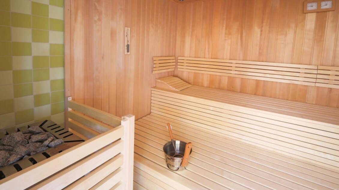 Eine helle Sauna mit Holzverkleidung und einem Steingitter. In der Ecke steht ein Eimer und eine Schaufel. | © Jufa Hotel Planneralm