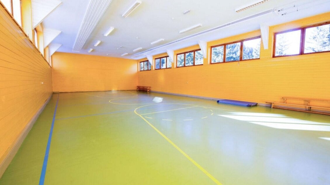 Ein heller Sportraum mit einem glatten, grünen Boden. Die Wände sind orange und große Fenster lassen viel Licht herein. | © Jufa Hotel Planneralm