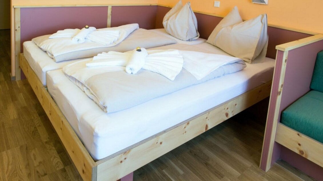 Ein gemütliches Doppelbett mit frischen Laken und Kissen. Der Raum hat eine helle, freundliche Atmosphäre und einen modernen Stil. | © Jufa Hotel Planneralm