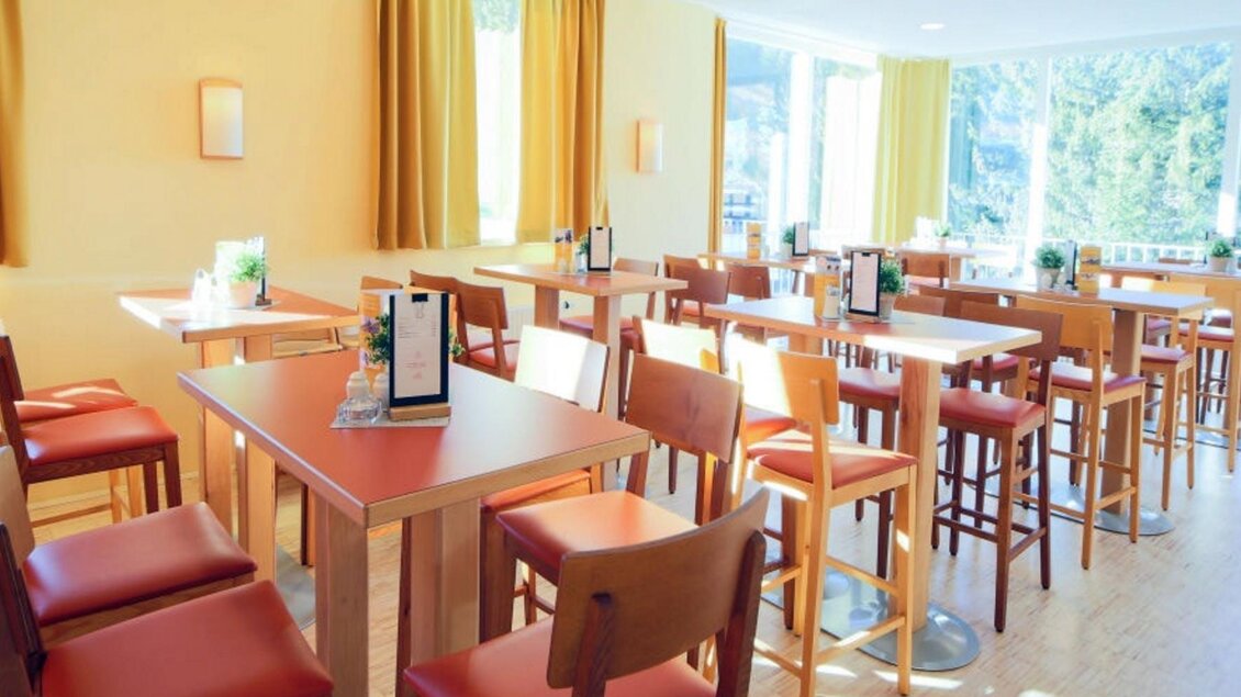 Ein helles Restaurant mit Holzstühlen und Tischen. Große Fenster lassen viel Licht hinein und geben einen Blick auf die Natur. | © Jufa Hotel Planneralm