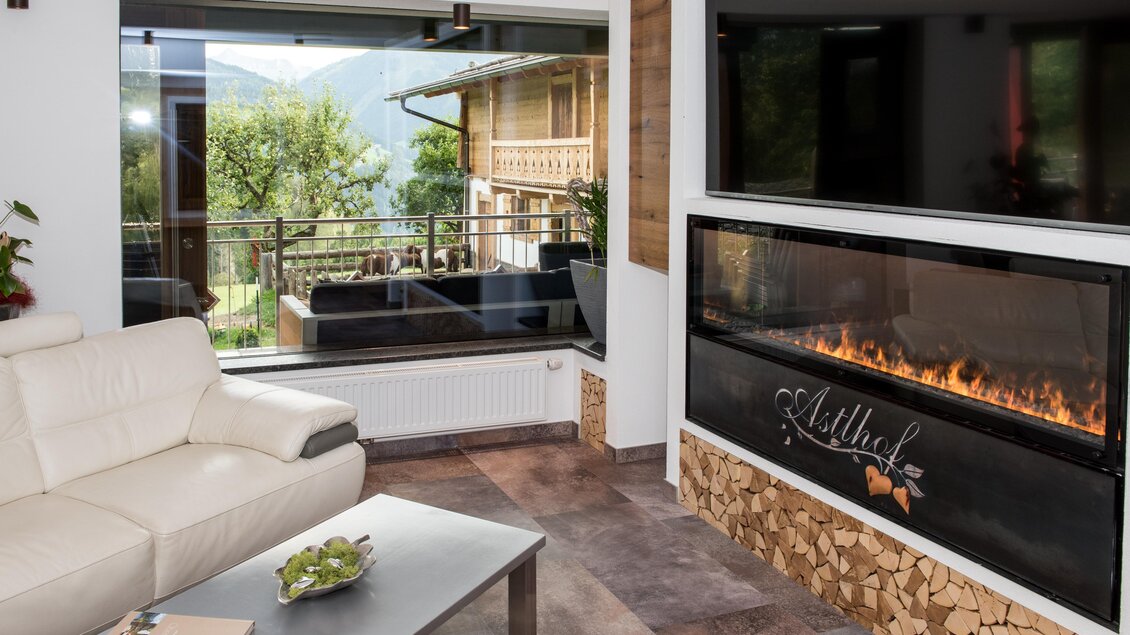 Ein modernes Wohnzimmer mit einem großen, offenen Kamin und einer gemütlichen Couch. Hinter dem Fenster sieht man eine schöne Aussicht auf die Berge und die Natur. | © Shooting Star