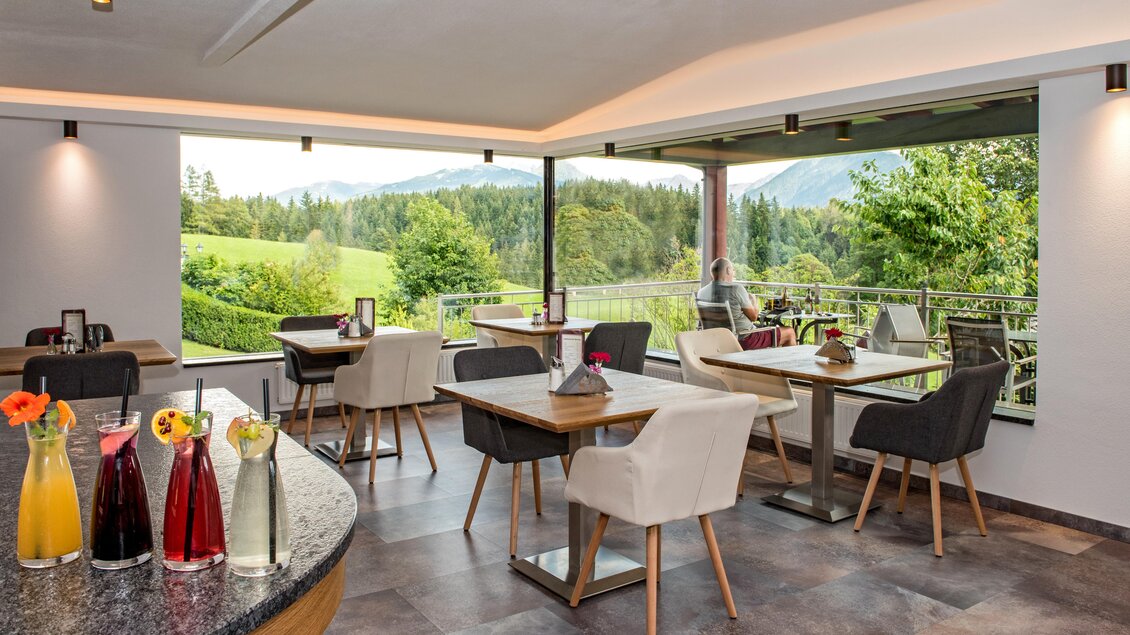 Ein helles Restaurant mit modernen Tischen und Stühlen. Große Fenster bieten einen Blick auf die grüne Landschaft und die Berge. | © Shooting Star