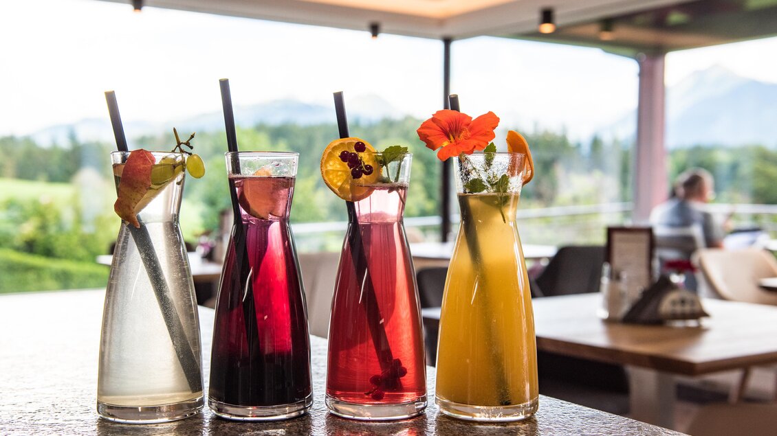 Vier bunte Cocktails stehen auf einem Tisch mit einer schönen Aussicht. Jeder Drink ist mit Früchten und Kräutern dekoriert. | © Shooting Star