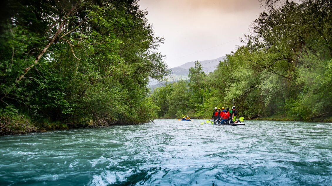 Eine Gruppe von Kajakfahrern paddelt auf einem klaren Fluss, umgeben von üppigem Grün und Bäumen. Die ruhige Wasseroberfläche spiegelt die natürliche Schönheit der Umgebung wider. | © Kajaktiv
