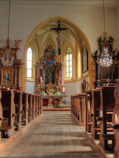 A beautiful interior of a church with wooden benches and ornate altars. The light streams through large windows and illuminates the space. | © Katholische Kirche