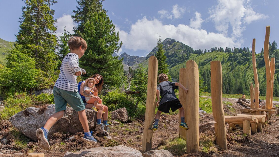 Eine Gruppe von Kindern spielt im Freien auf einem Abenteuer-Spielplatz. Die Landschaft ist grün mit Bergen im Hintergrund und einem blauen Himmel. | © Hauser Kaibling