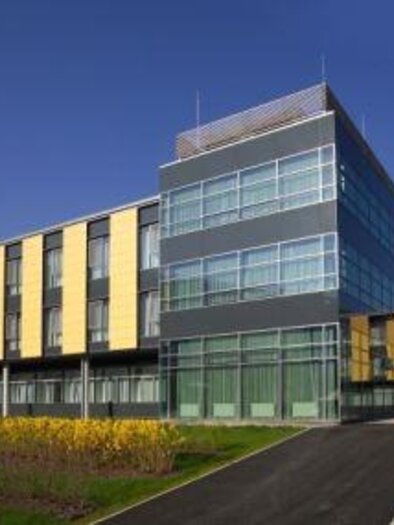 A modern building with large windows and yellow accents. The surroundings are well-maintained with green lawns and trees. | © Klinik Diakonissen Schladming