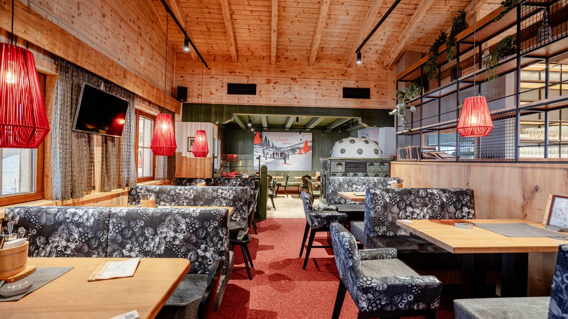 Ein gemütliches Restaurant mit Holzelementen und modernen Möbeln. Rote Lampen und große Fenster sorgen für eine einladende Atmosphäre. | © Knapplhütte