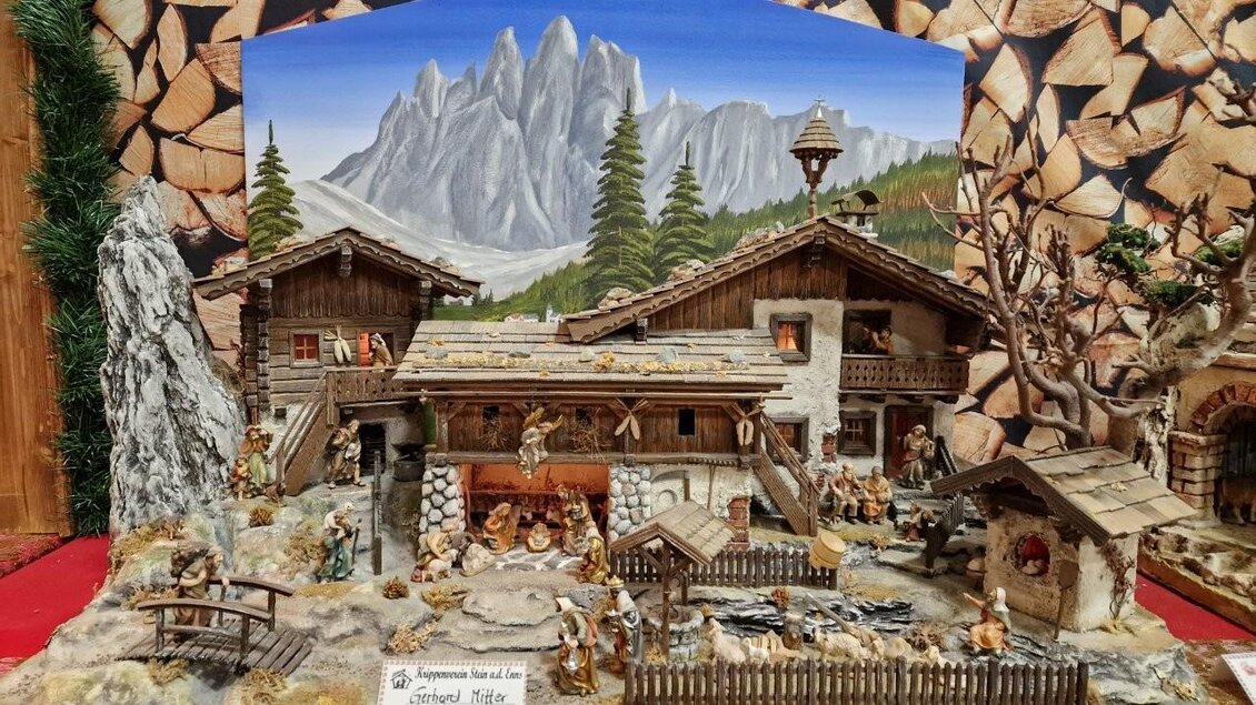 Eine reizvolle Weihnachtskrippe mit Häusern in Alpenstil und vielen Figuren. Im Hintergrund sind majestätische Berge und grüne Tannenbäume zu sehen. | © Gerald Gerhardter