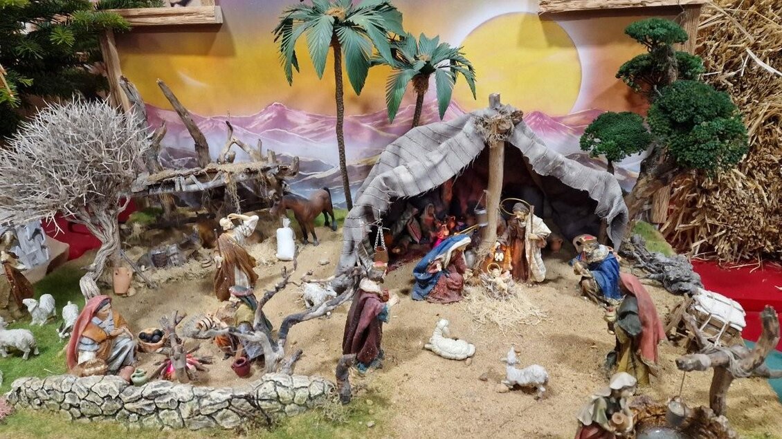 Eine Krippe mit Figuren aus der Weihnachtsgeschichte, die um ein Feuer versammelt sind. Im Hintergrund sind Palmen und eine farbenfrohe Landschaft zu sehen. | © Gerald Gerhardter