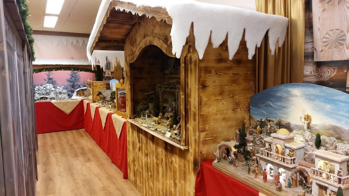 Ein festlich dekorierter Weihnachtsmarktstand mit Holzverkleidung und schneebedecktem Dach. Im Inneren sind verschiedene Weihnachtskrippen und Figuren ausgestellt. | © Gerald Gerhardter