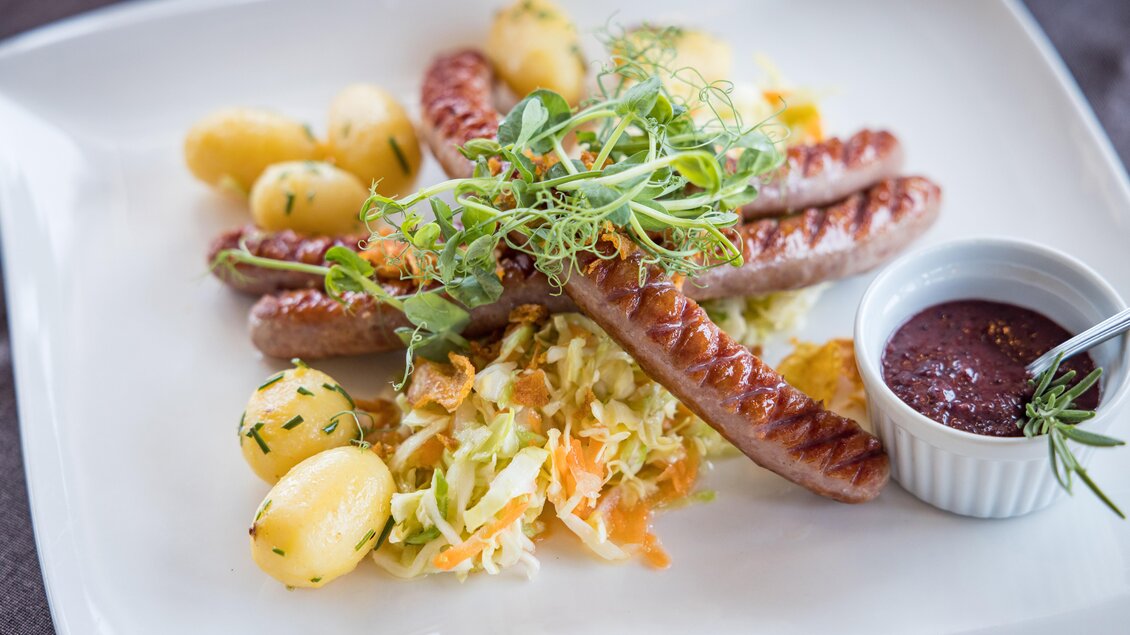 Ein Teller mit gegrillten Würstchen, Kartoffeln und einem frischen Krautsalat. Dazu gibt es eine kleine Schüssel mit Sauce. | © Netzwerk Kulinarik wildbild