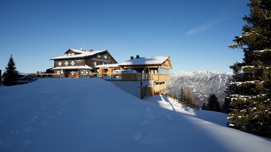 Ein malerisches Gebäude in schneebedeckter Landschaft. Die klare Aussicht auf die Berge und der blaue Himmel schaffen eine winterliche Atmosphäre. | © Krummholzhütte