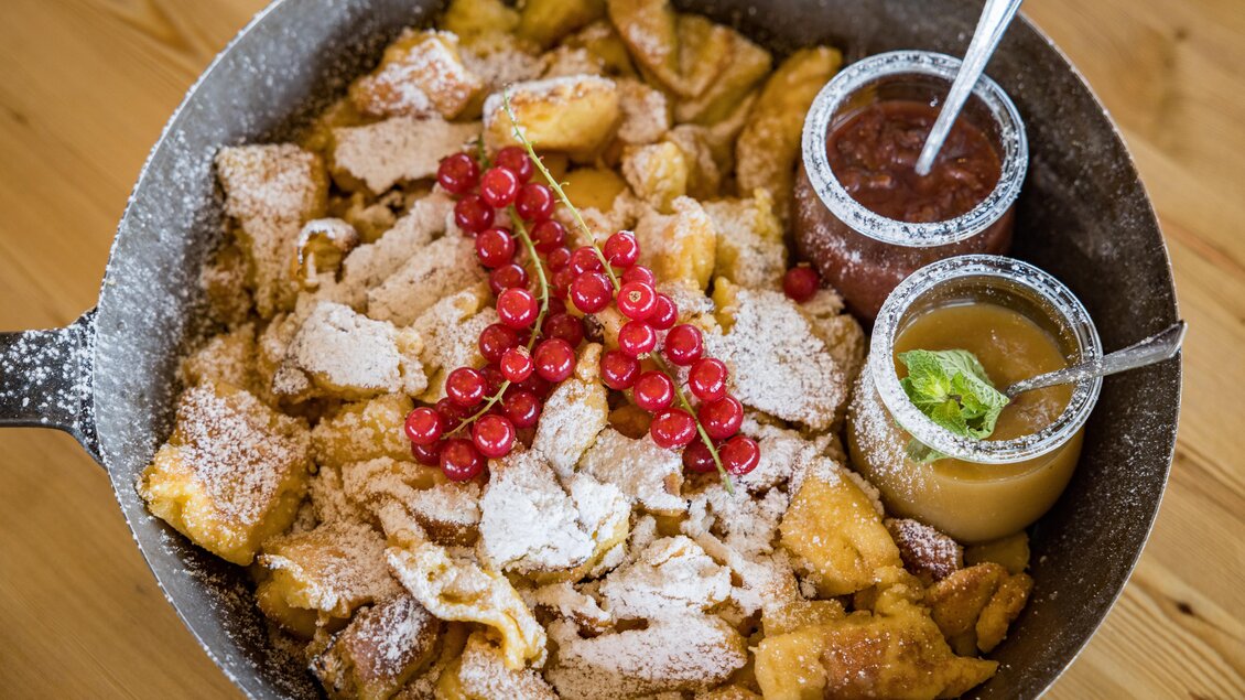 Ein köstlicher Kaiserschmarrn mit Puderzucker, garniert mit roten Johannisbeeren. Dazu gibt es zwei süße Saucen in Schalen. | © Netzwerk Kulinarik wildbild