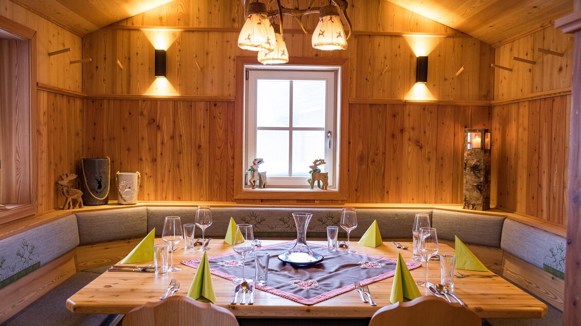 Ein gemütlicher Speisesaal aus Holz mit einer runden Tischanordnung. Auf dem Tisch stehen Gläser und gelbe Servietten, während sanftes Licht den Raum beleuchtet. | © Netzwerk Kulinarik wildbild