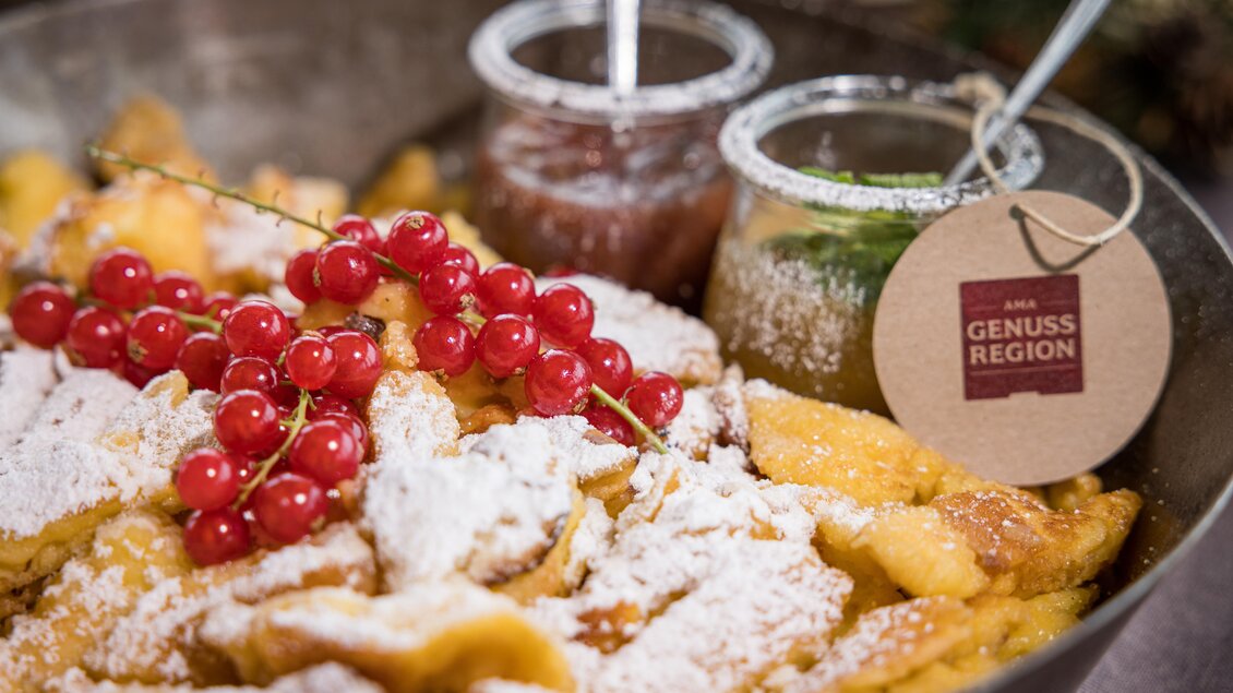 Ein köstlichesDessert aus gebackenem Teig, garniert mit Puderzucker und roten Johannisbeeren. Dazu serviert werden zwei verschiedene Saucen in gläsernen Behältern. | © Netzwerk Kulinarik wildbild