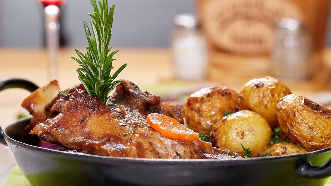 Ein leckeres Gericht mit saftigem Fleisch, gewürzt und mit frischen Kräutern garniert. Dazu zarte, goldene Kartoffeln auf dem Tisch serviert. | © Birgit Steinberger