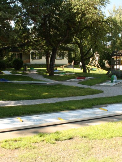 A spacious outdoor area with lawns, trees, and various play options. In the background, a playground and a house are visible. | © TVB Gröbminger Land 