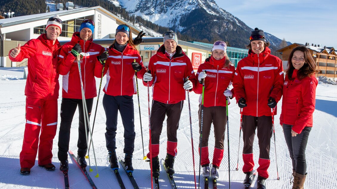Eine Gruppe von sieben Skifahrern steht auf einer schneebedeckten Fläche. Sie tragen rote Skijacken und glückliche Gesichter vor einer malerischen Bergkulisse. | © Langlaufschule Ramsau