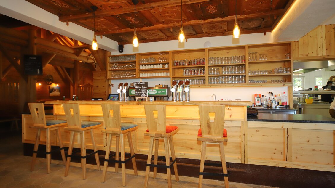 Eine gemütliche Bar mit Holzregalen und Hockern. Die Theke ist gut beleuchtet und bietet verschiedene Getränke an. | © Gerald Petter