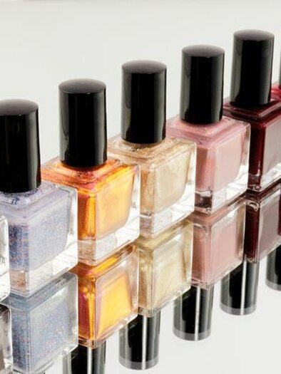 A row of nail polish bottles in different colors is standing on a mirror. The bottles are arranged in a line and are reflecting each other. | © Margit Hubner Kosmetik-Fußpflege-Massage 