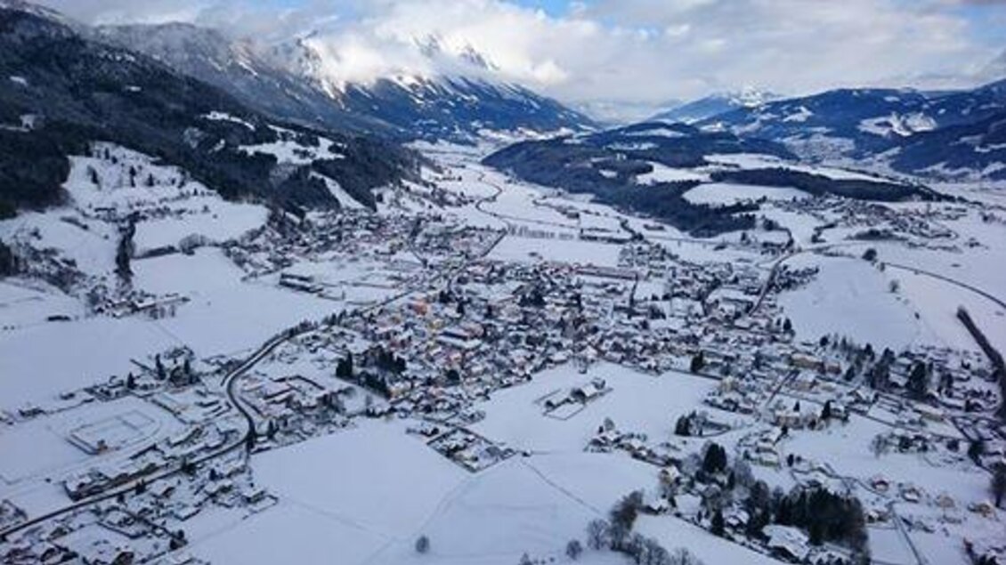 Eine winterliche Landschaft mit einer kleinen Stadt, die von Schnee bedeckt ist. Die Berge im Hintergrund verleihen der Szene eine malerische Atmosphäre. | © Thomas Reingruber